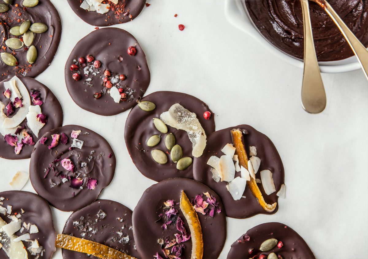 Dark chocolate discs topped with pumpkin seeds, orange and rose petals.