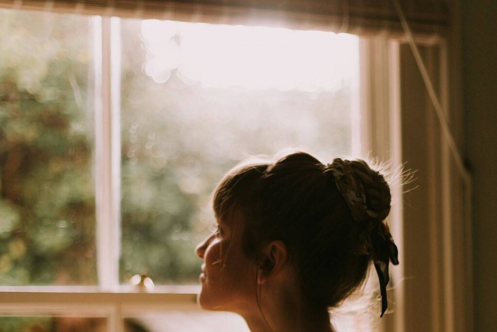 A woman holding a warm mug by a sunlit window.