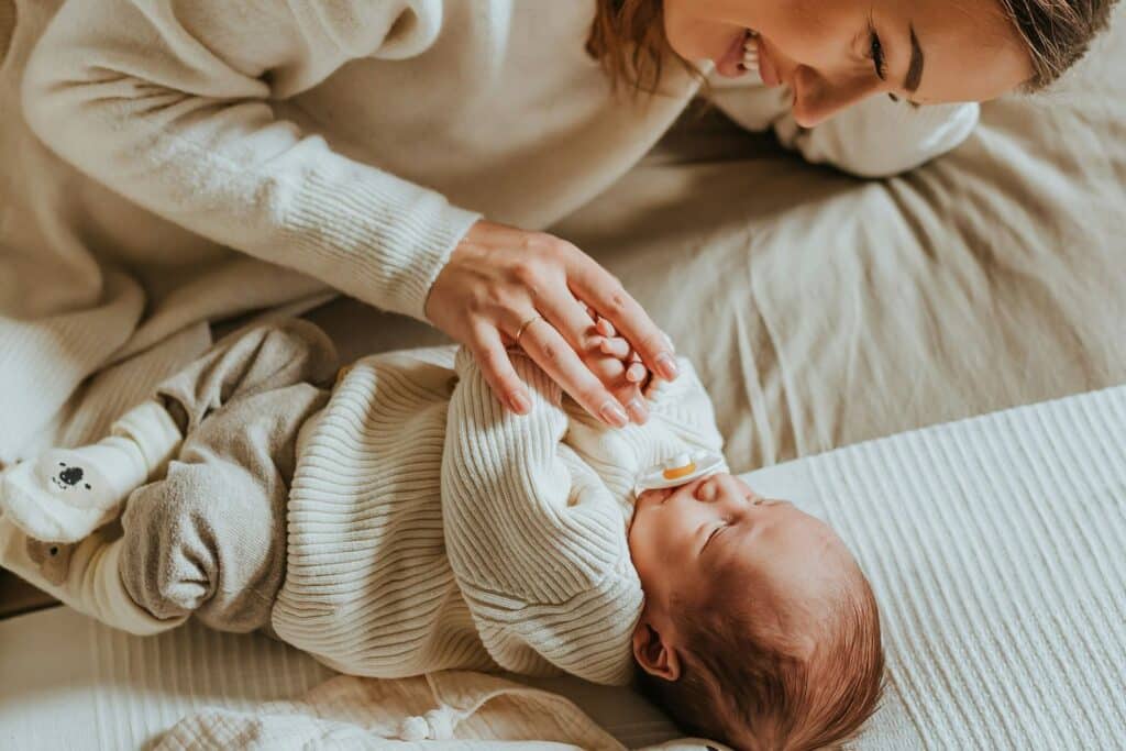 A mother lying beside her newborn baby on a bed in soft light.