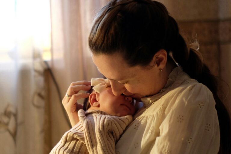 A mother holding her newborn close by a softly lit window.