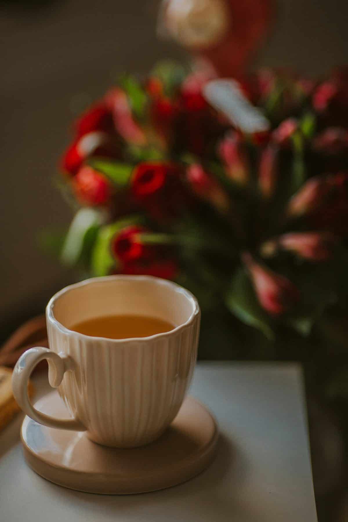 A cup of tea beside a vase of tulips in soft light.