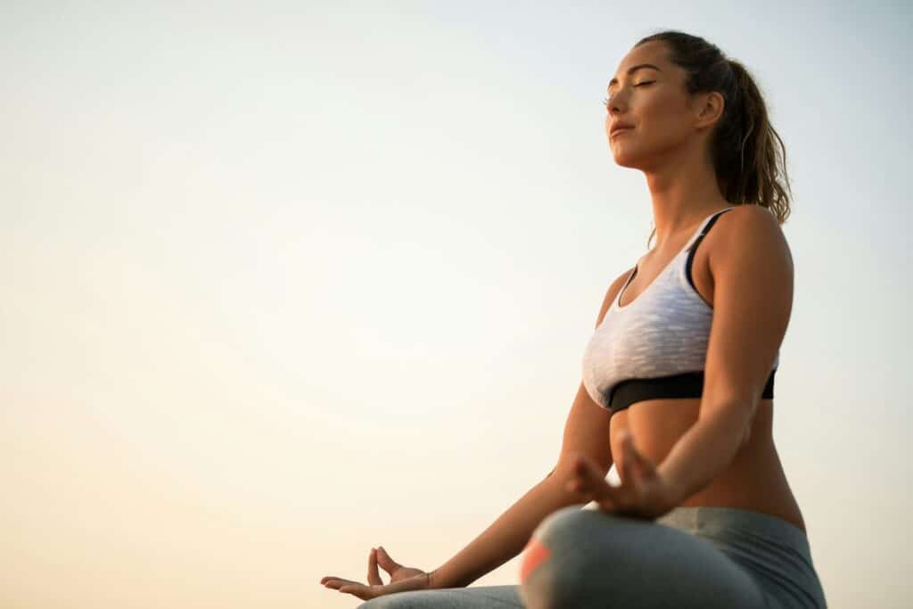 A woman sitting cross-legged with her hands resting gently, breathing in warm light.