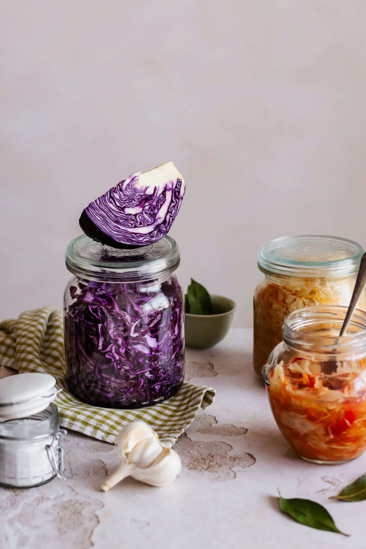 Jars of fermented food, including sauerkraut and kimchi, lined up on a shelf.