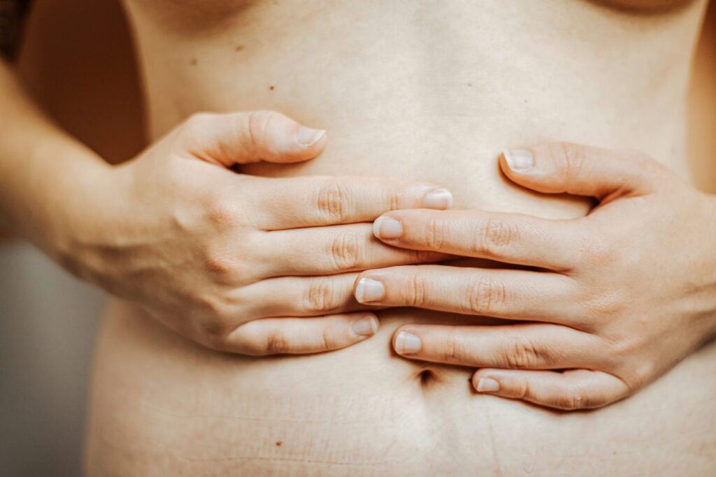 A woman gently holding her bare stomach, representing gut health and digestion.