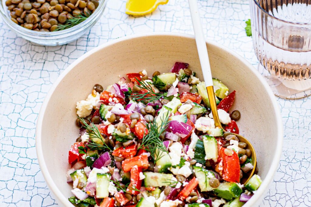 A bowl of lentil salad with fresh vegetables and herbs.