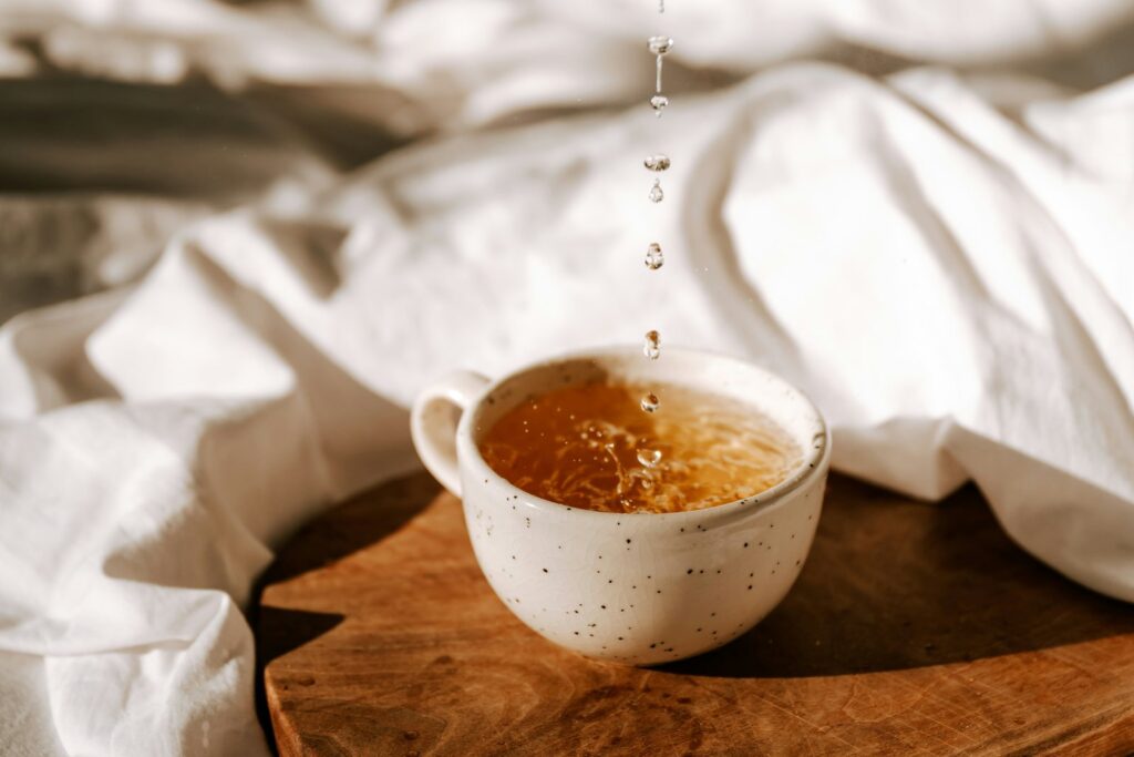 Honey drizzling into a warm cup of tea on a wooden board.