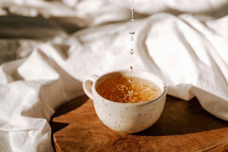 Honey drizzling into a warm cup of tea on a wooden board.