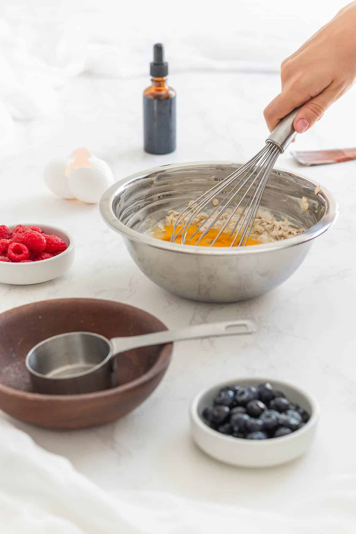 A person preparing bowls of oats with blueberries, whisking them in the kitchen.