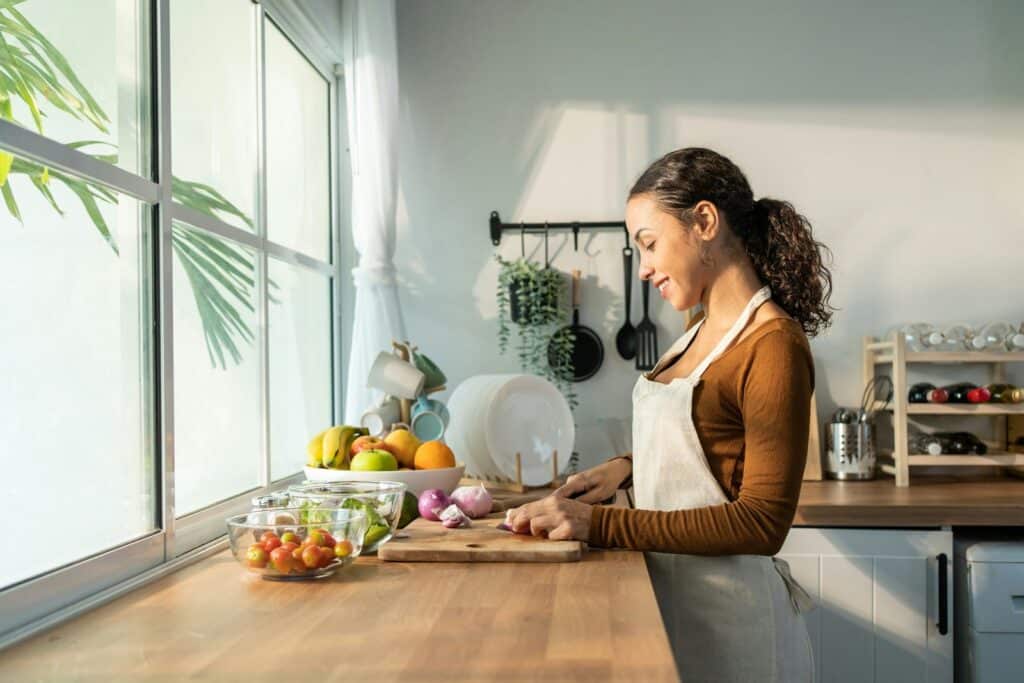 A woman preparing fresh food at a sunny kitchen counter.
