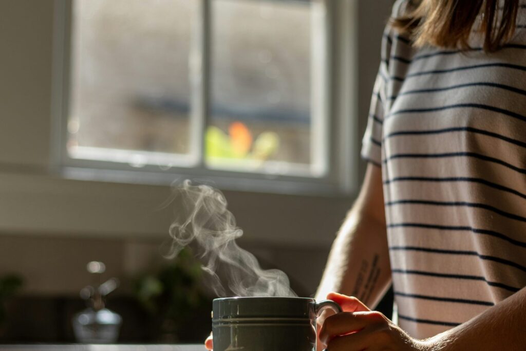 A woman sitting at a table with a steaming mug in soft morning light.