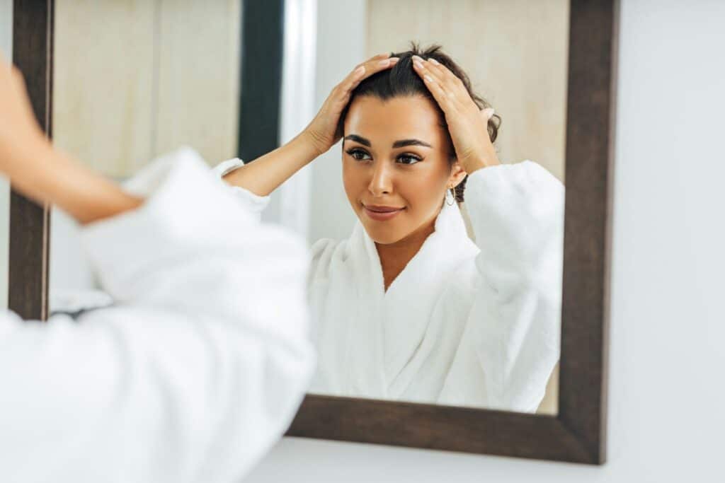 A woman in a robe running her hands through her hair in front of a mirror.