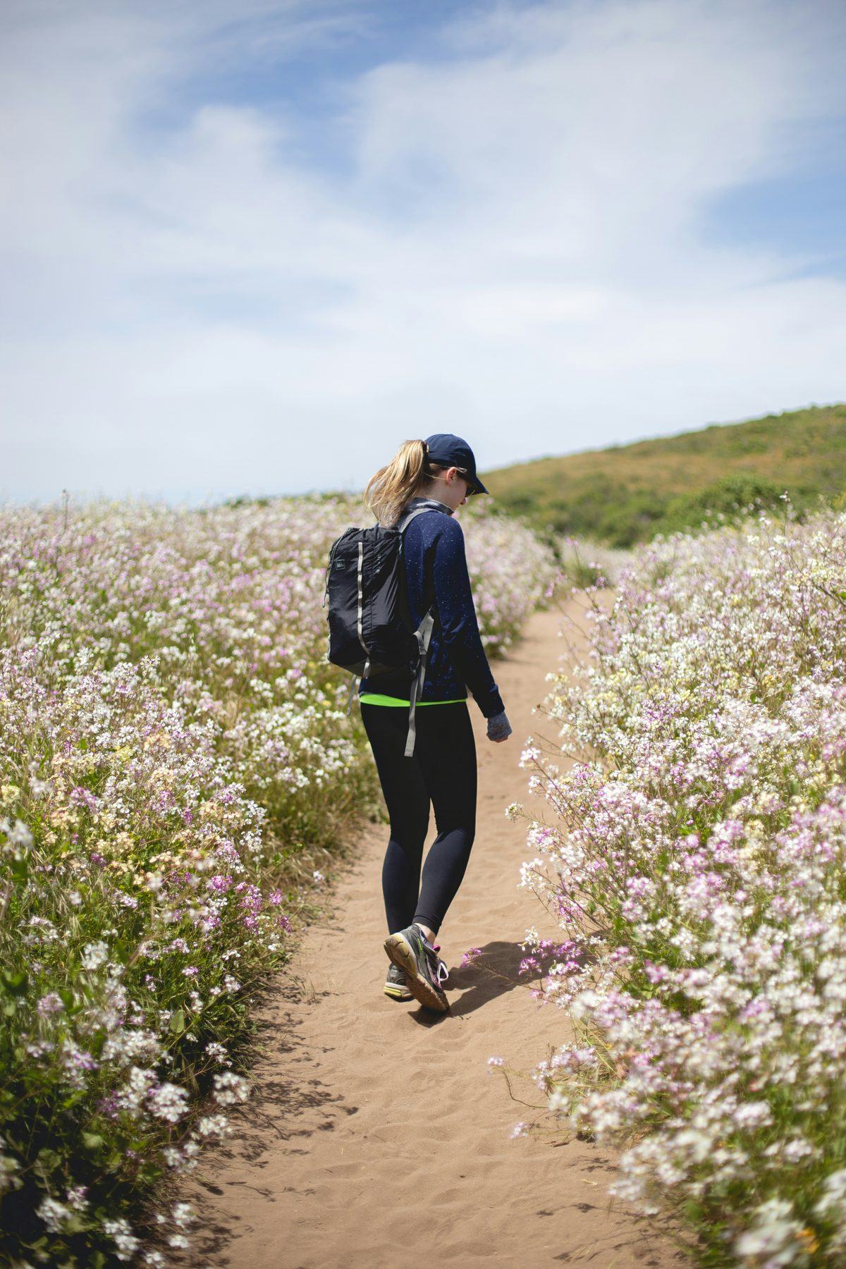 A woman walking along a coastal path lined with wildflowers.
