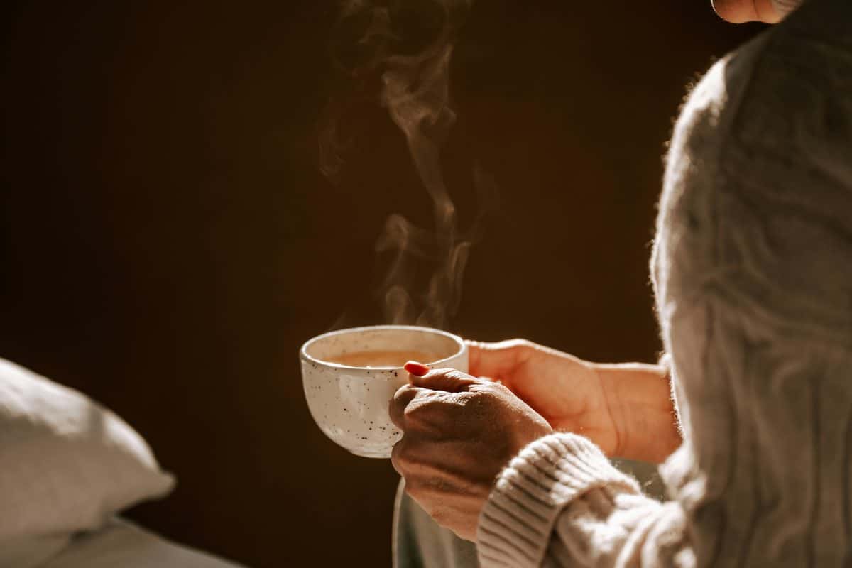 Hands holding a steaming cup in soft evening light.