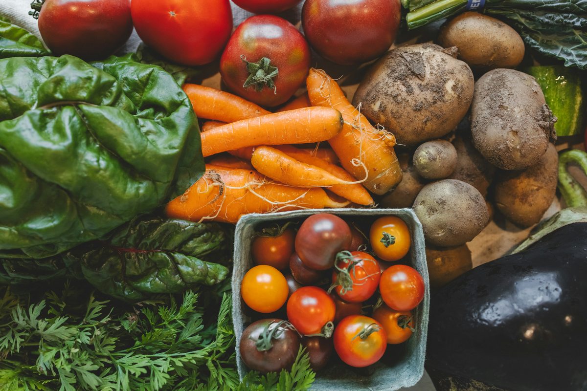 A crate of fresh vegetables including peppers, carrots and tomatoes.